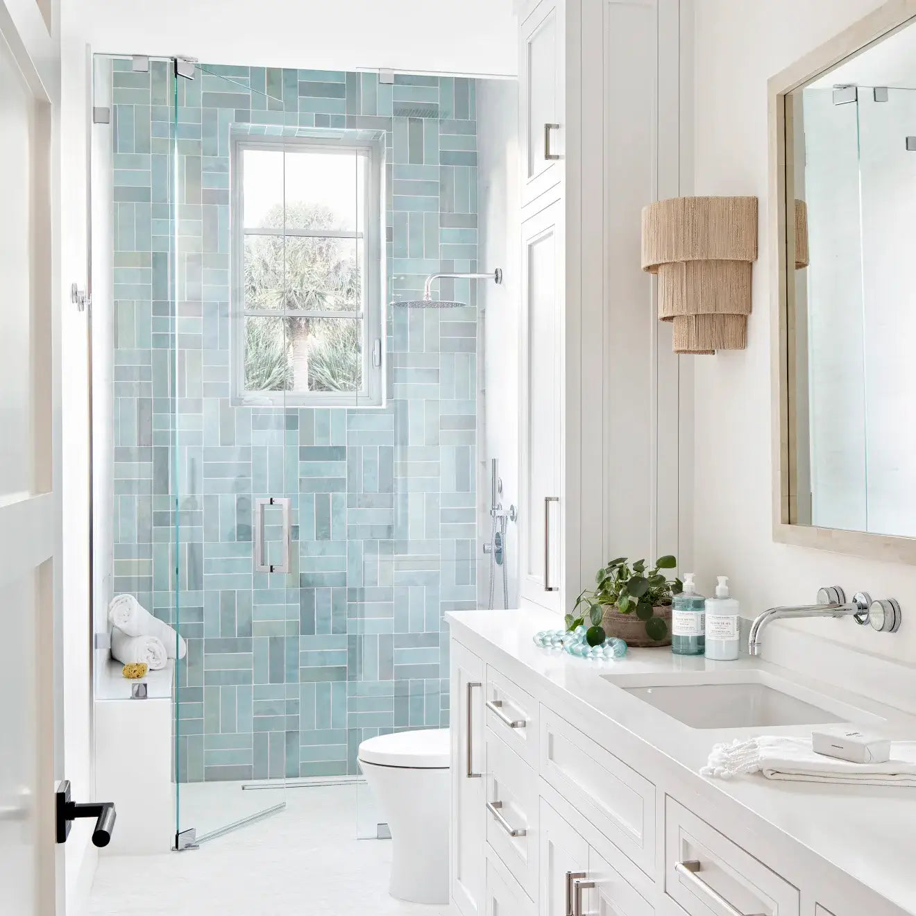 Modern bathroom featuring a glass shower with blue-green tile, white cabinetry, and natural decor for a fresh, airy ambiance.