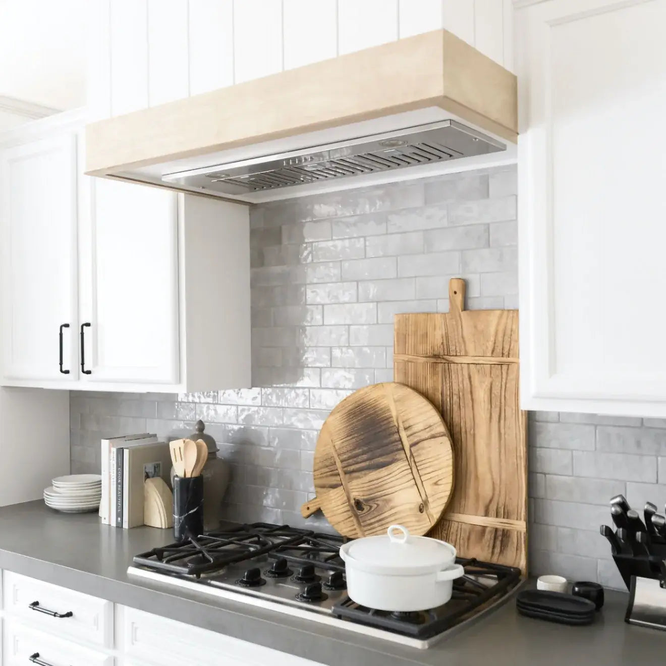 Modern kitchen with grey glossy ceramic tiles, wooden cutting boards, and a stainless steel hood above the gas stove.