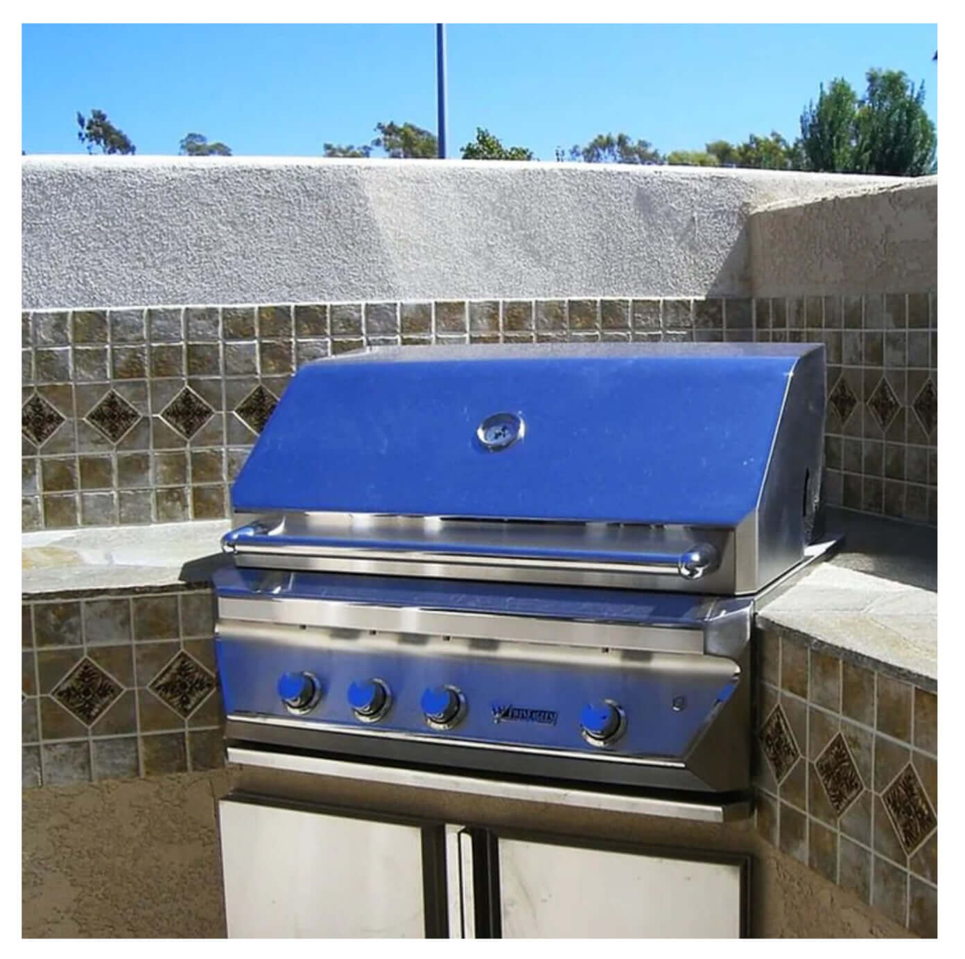Stainless steel outdoor gas grill with shiny surface on a tiled counter.
