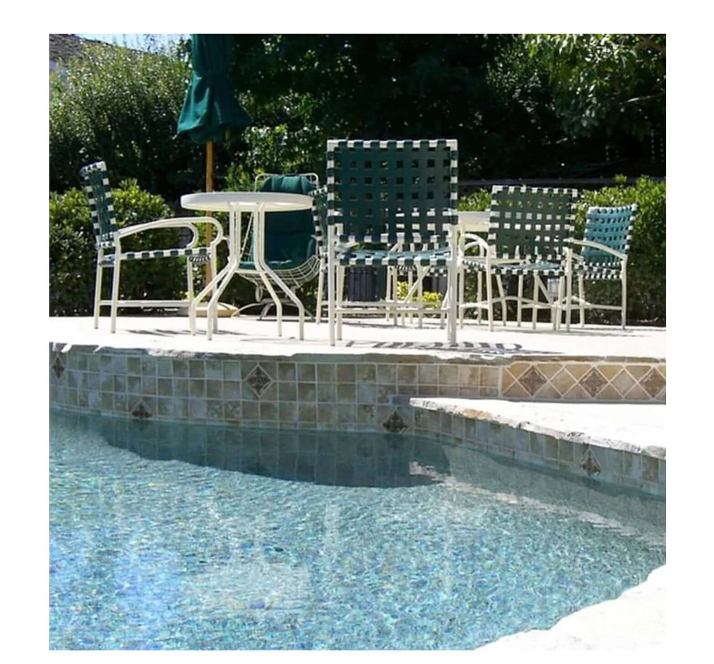 Poolside seating area with green chairs and a table beside a sparkling blue pool.