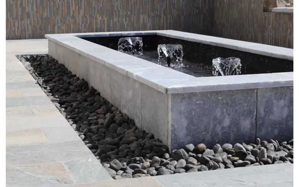 Modern outdoor water feature with fountains surrounded by stone and paver stones, enhancing the landscape design.