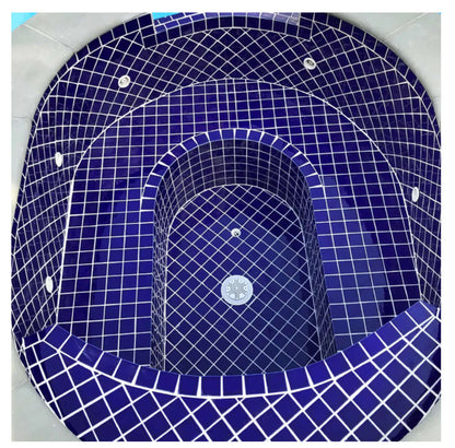 Top view of a cobalt blue mosaic tiled hot tub, featuring a sleek oval design with modern plumbing fixtures.