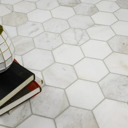 5" Arabescato Venato White Hexagon Mosaic Tile flooring with stacked books and decor, elegant interior design.
