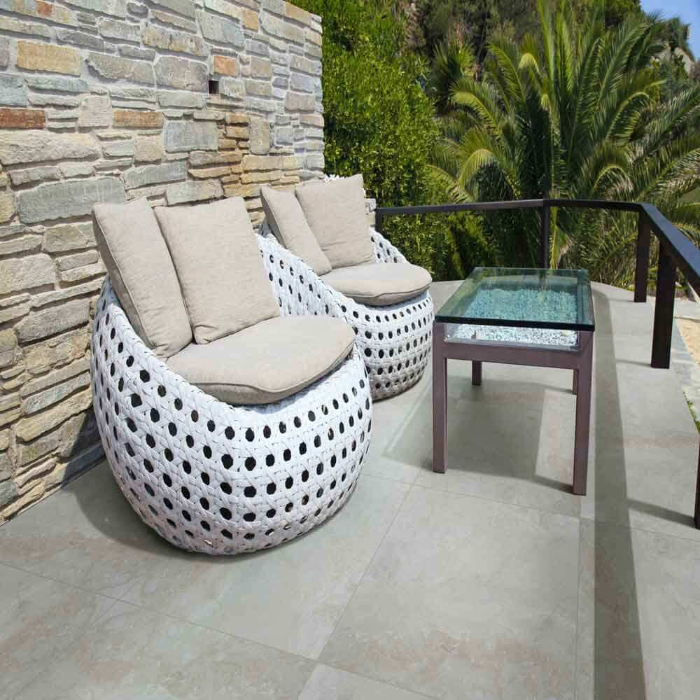 Outdoor seating area featuring two stylish white woven chairs and a glass table on a stone patio.